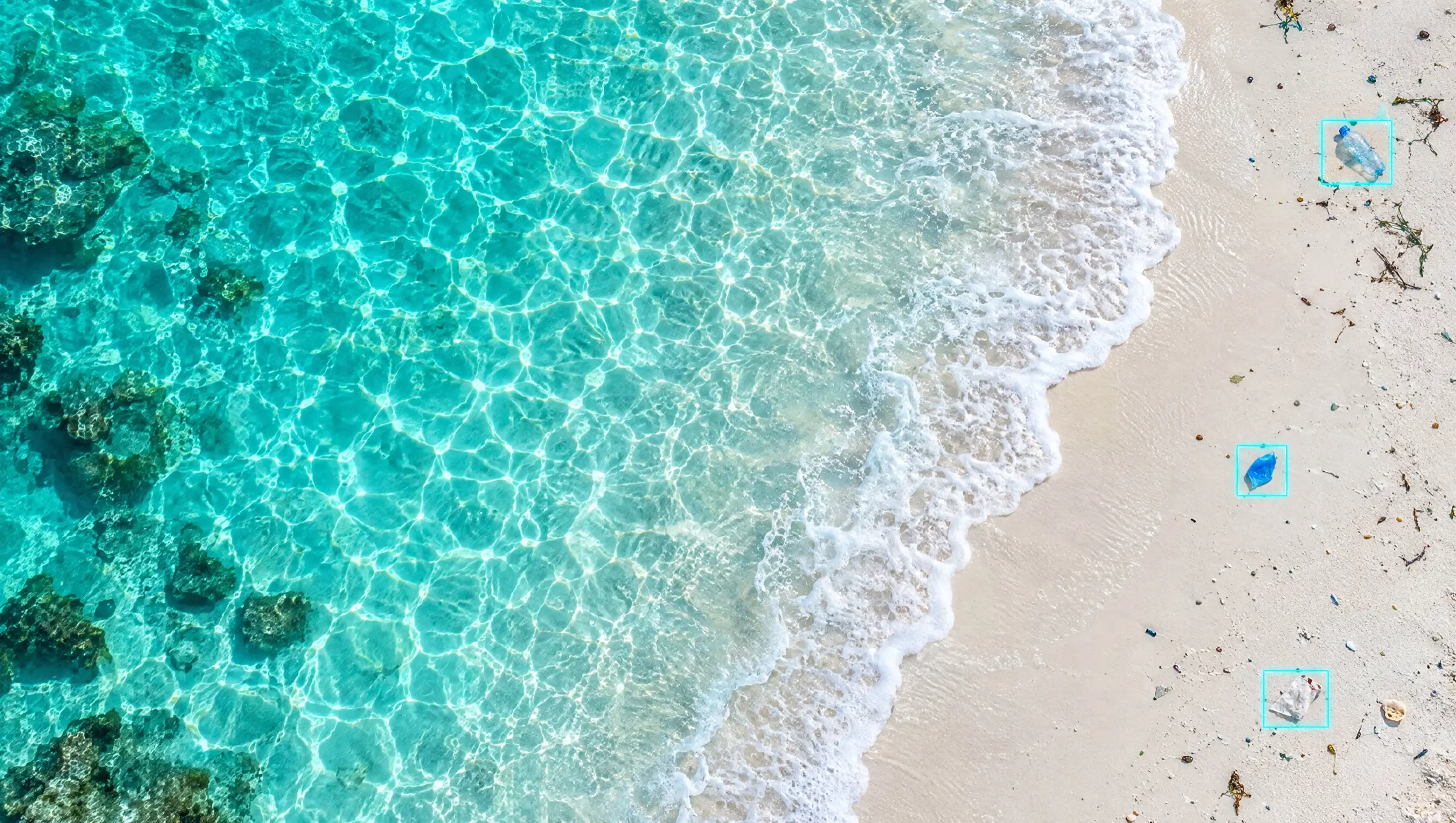 Turquoise shallows and white sand from above, three small pieces of litter each enclosed in a thin detection box